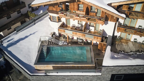 A multi-story wooden chalet with a swimming pool, balconies, and a ski slope in the background. - Hotel Astrid mit Panoramapool & inklusive JokerCard (Saalbach-Hinterglemm)