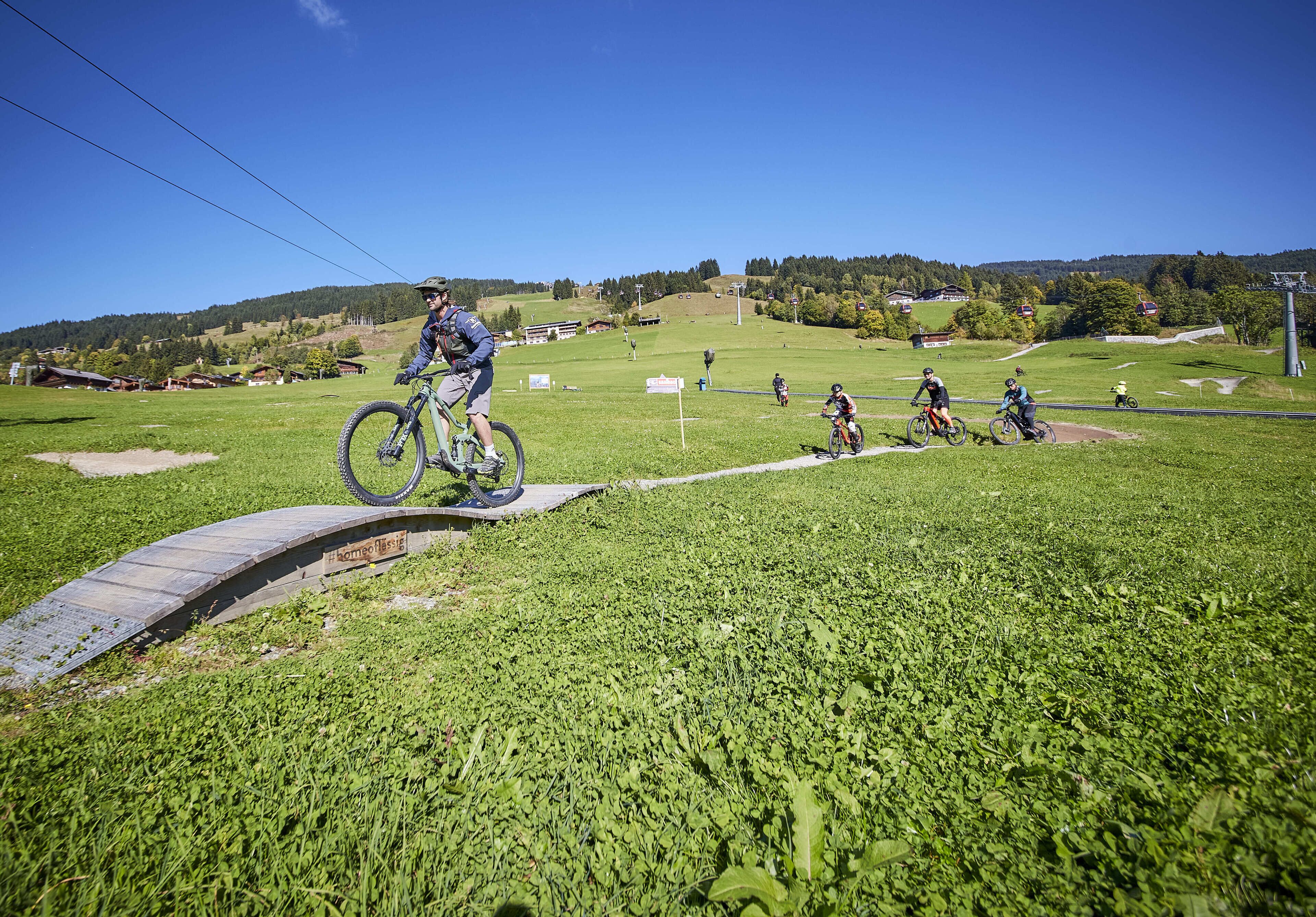 Ein Mountainbike-Weg mit einer Holzbrücke und grasbewachsenem Gelände.