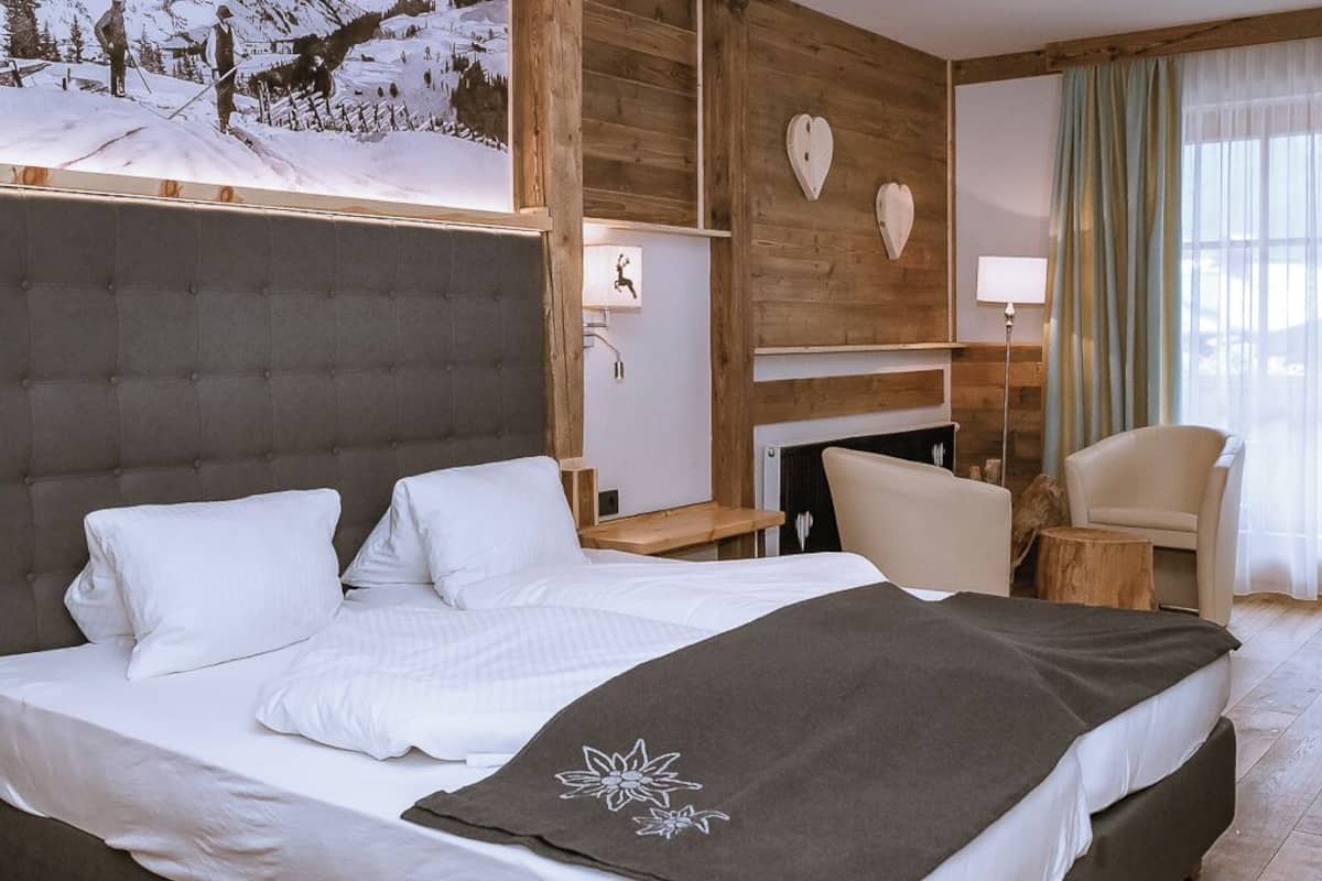 A hotel room with a large bed, a wooden headboard, a fireplace, a chair, and a view of a snowy landscape.