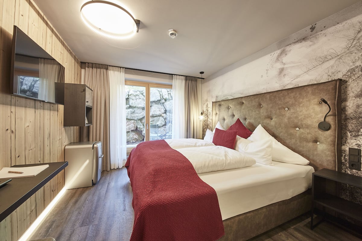 A modern bedroom with a large bed, a small bedside table, a built-in TV, and a stone wall.