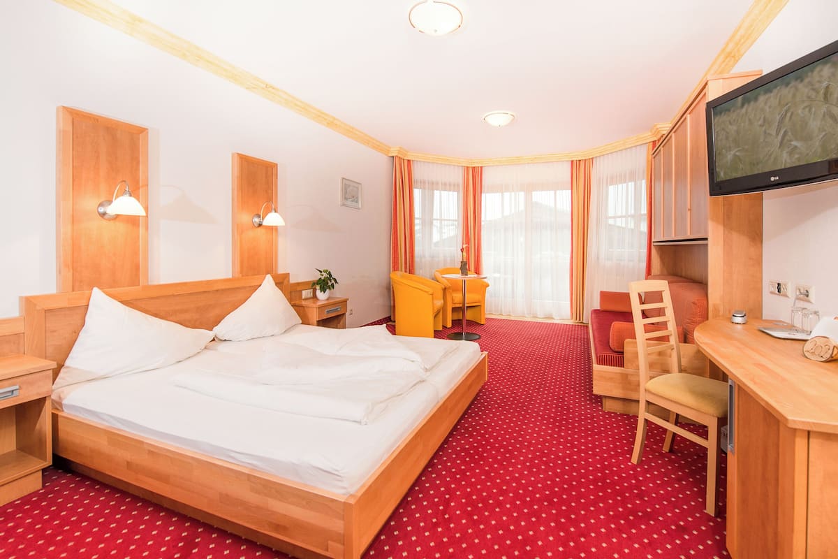 A hotel room with a wooden bed, a desk with a chair, a television, and a red carpeted floor.
