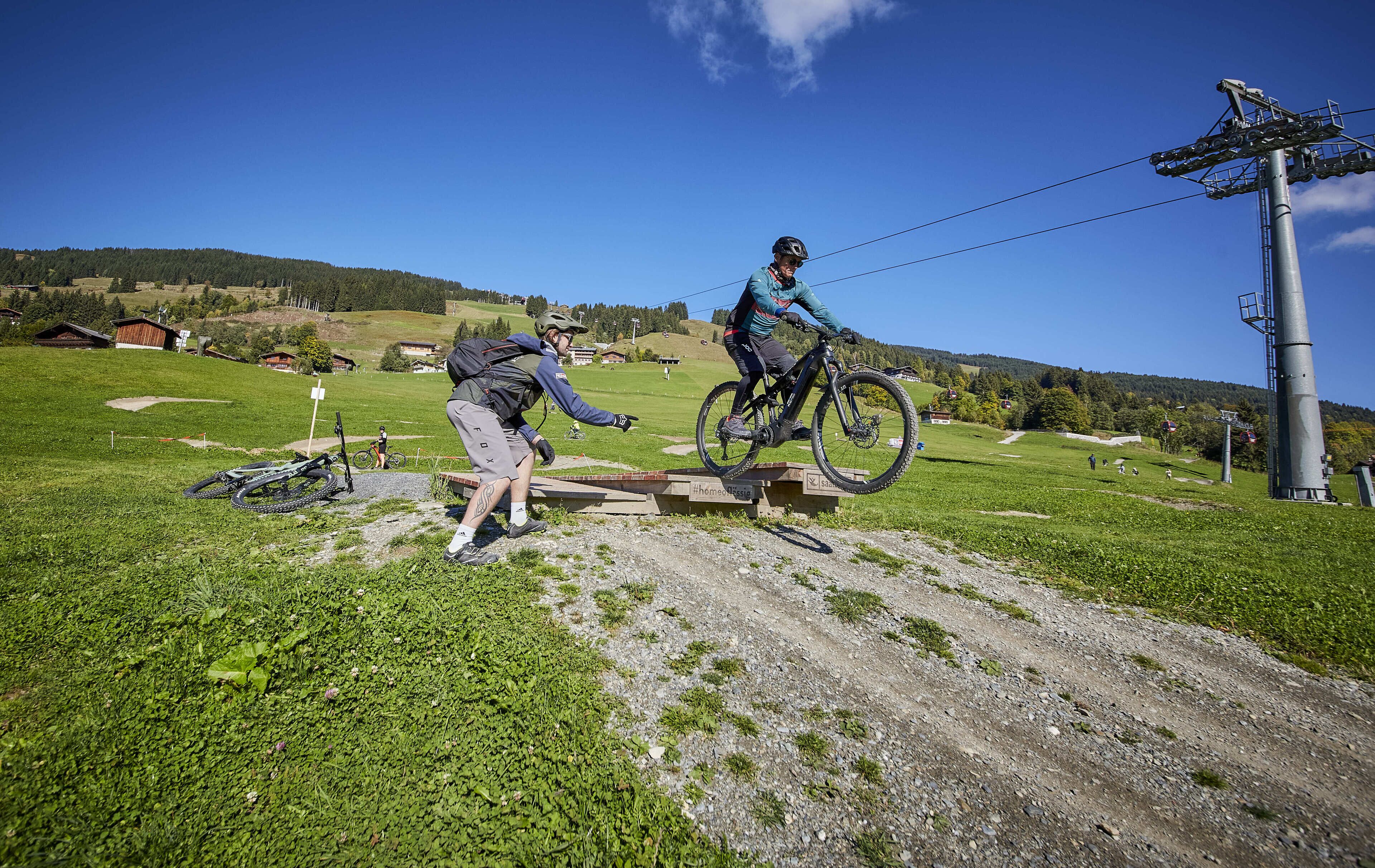 Een mountainbiketrail met een houten sprong en een fietser in de lucht.