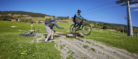 Een mountainbiketrail met een houten sprong en een fietser in de lucht.