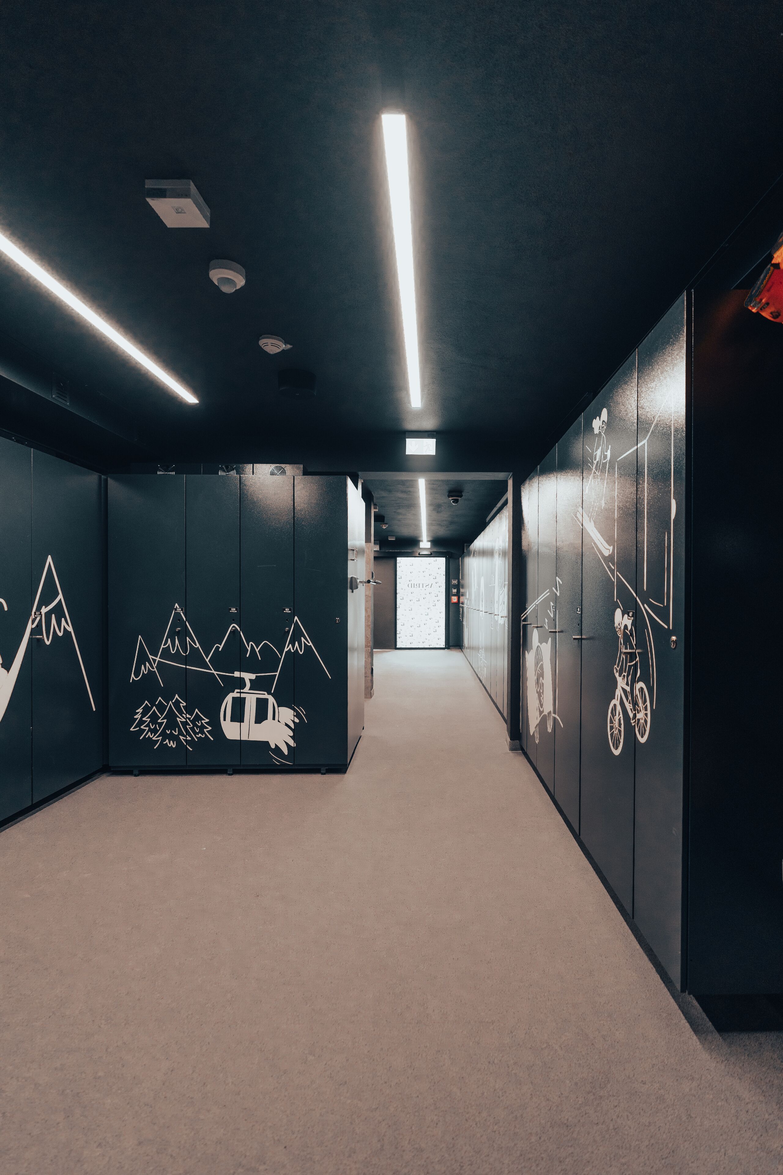 A hallway with dark walls, ceiling lights, and a distant view of a room.