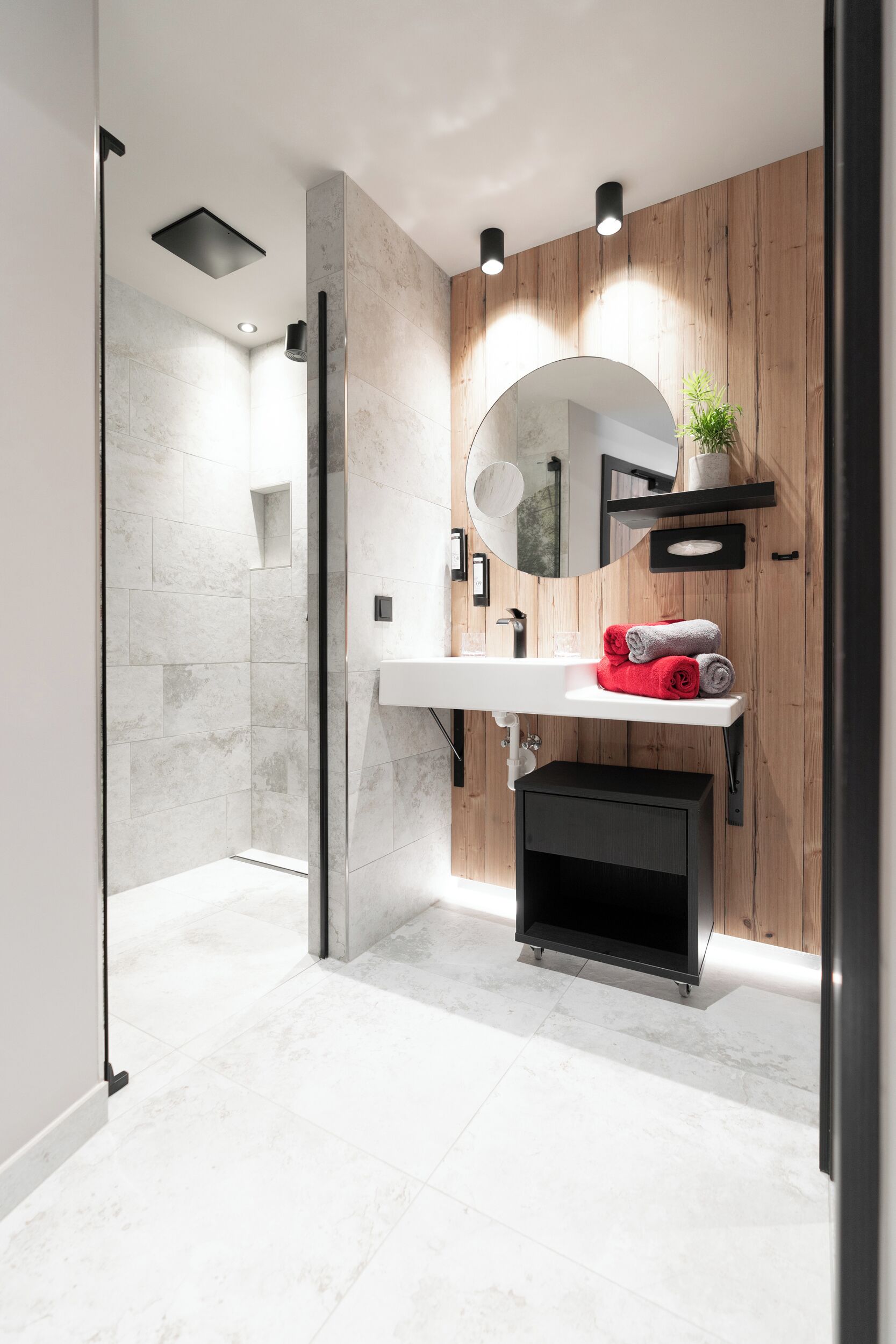 A modern bathroom with a glass-enclosed shower, a white sink with a mirror, and wooden paneling on the walls.