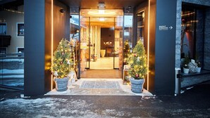 De ingang van Hotel Astrid, met een stenen gevel, een bord boven de deur en twee kerstbomen in potten.