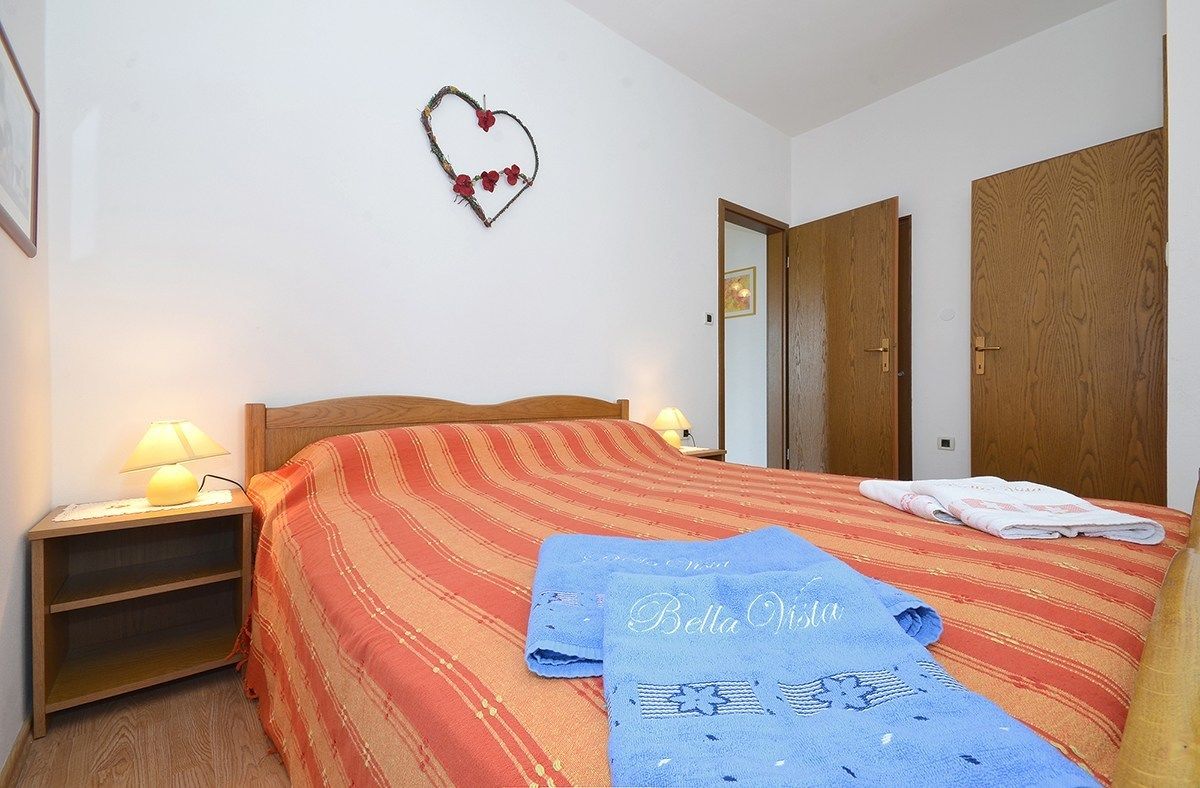 A bedroom with a bed, two bedside lamps, a heart-shaped decoration, and a blue towel with text.