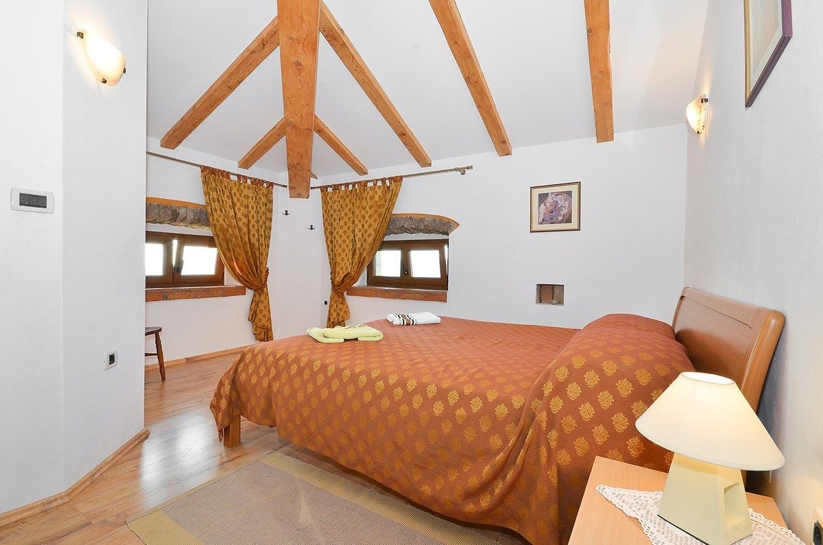 A bedroom with a wooden ceiling, a bed with a patterned bedspread, a nightstand with a lamp, and a window with curtains.