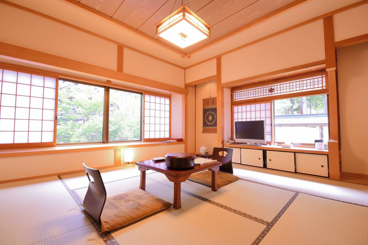 A traditional Japanese room with tatami flooring, a low table with a pot, a chair, and a television.