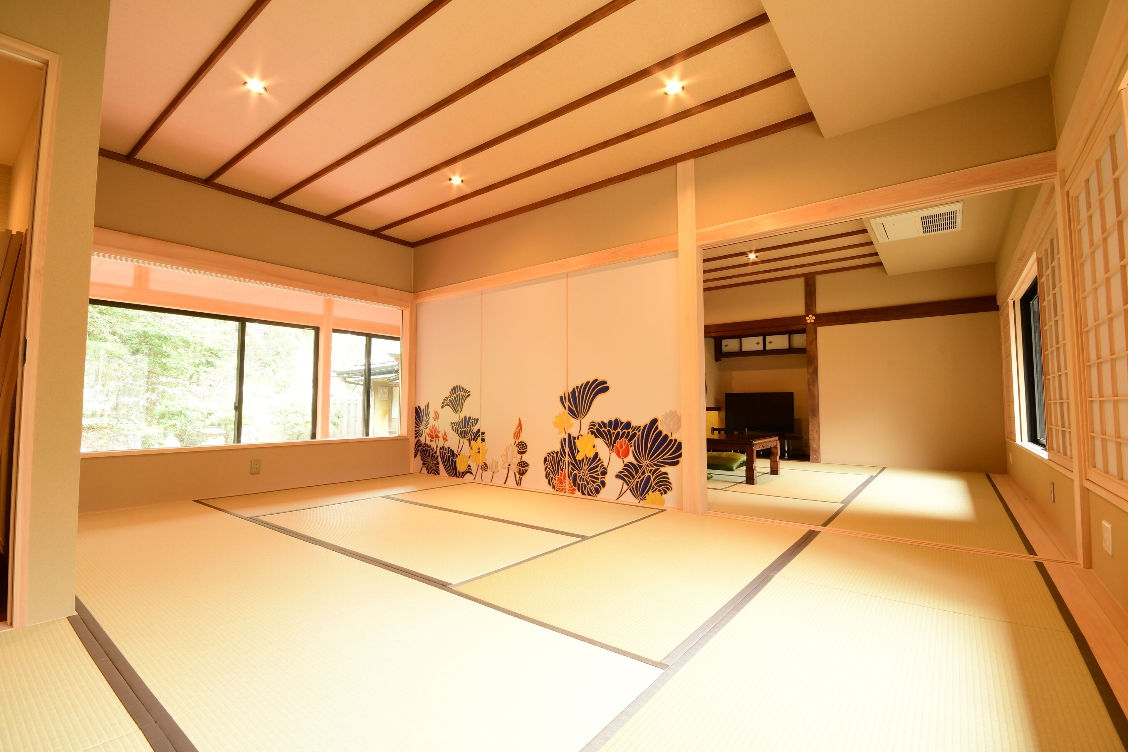 A tatami mat room with wooden beams, large windows, and a traditional Japanese sliding door.