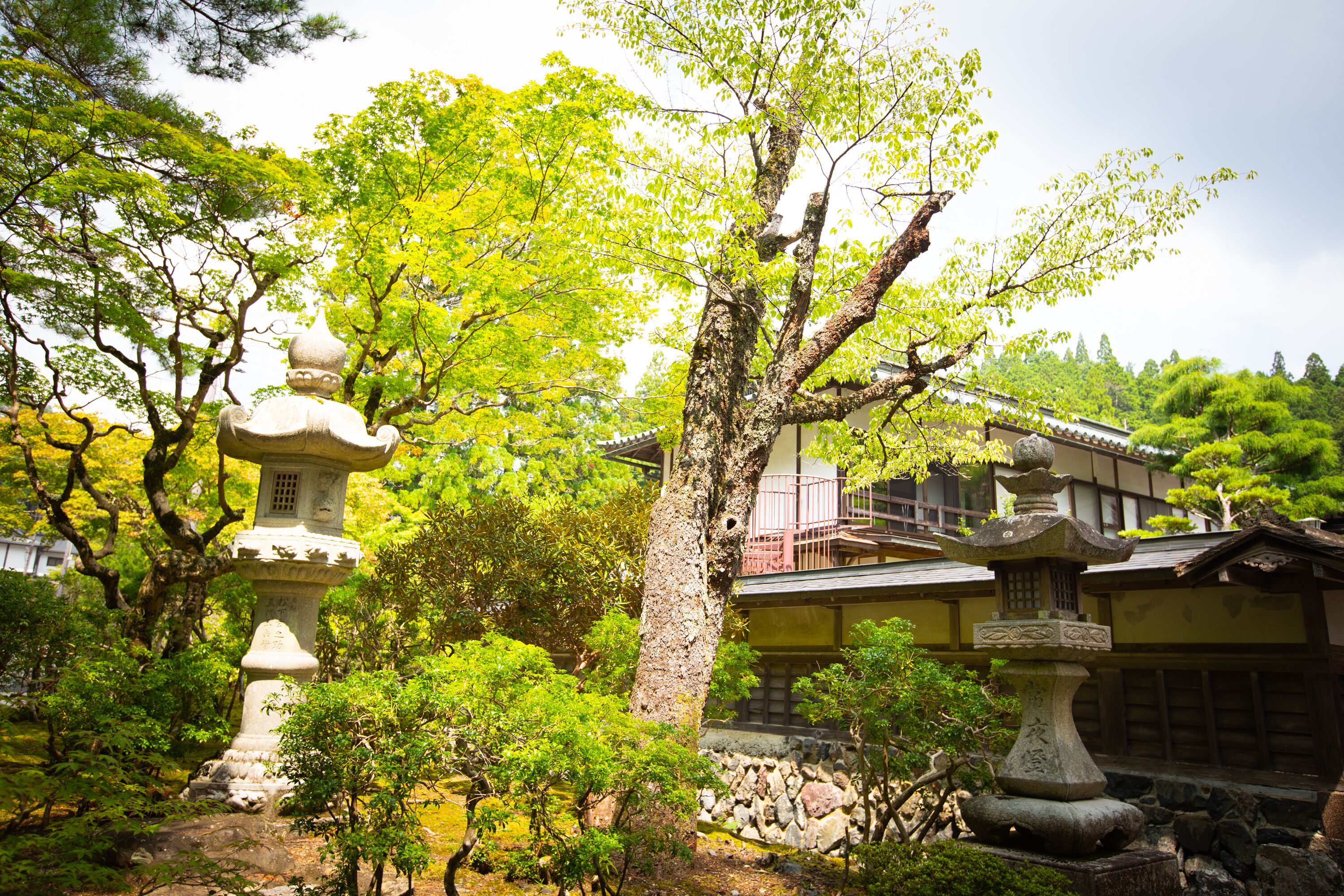 A traditional Japanese garden with stone lanterns and a building with a tiled roof.