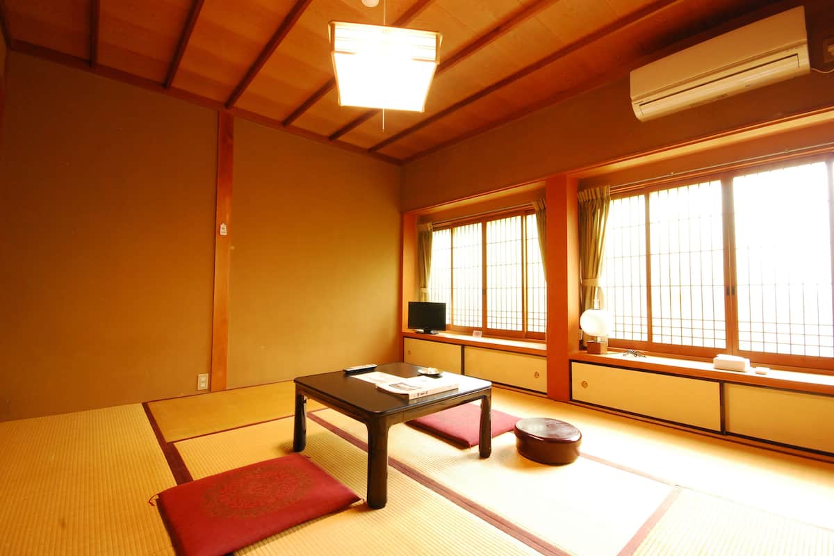 A traditional Japanese room with tatami flooring, a low table with cushions, a television, and a window with curtains.