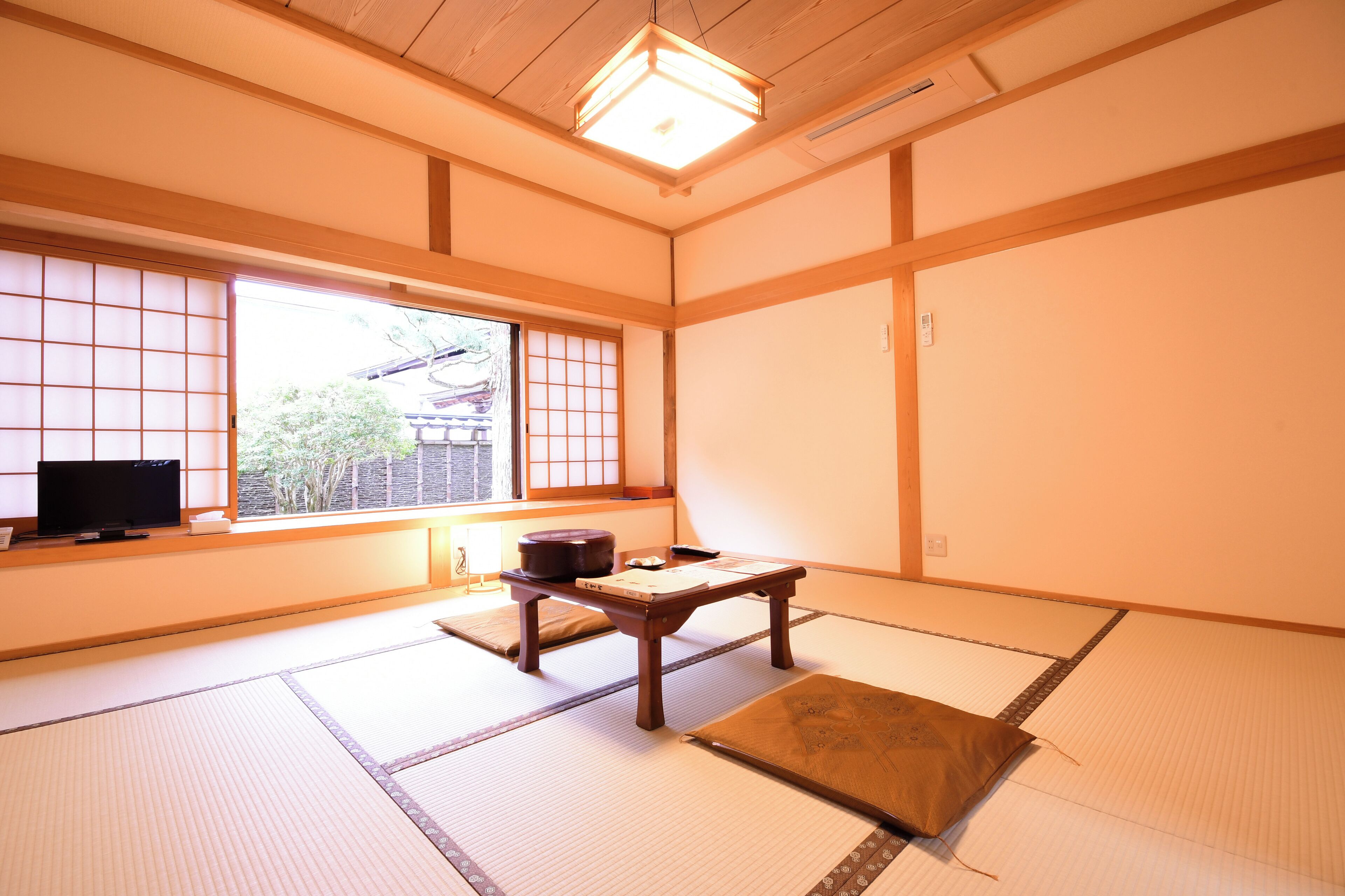 A traditional Japanese room with tatami flooring, a low wooden table, a television, and a window with a view of a traditional building.