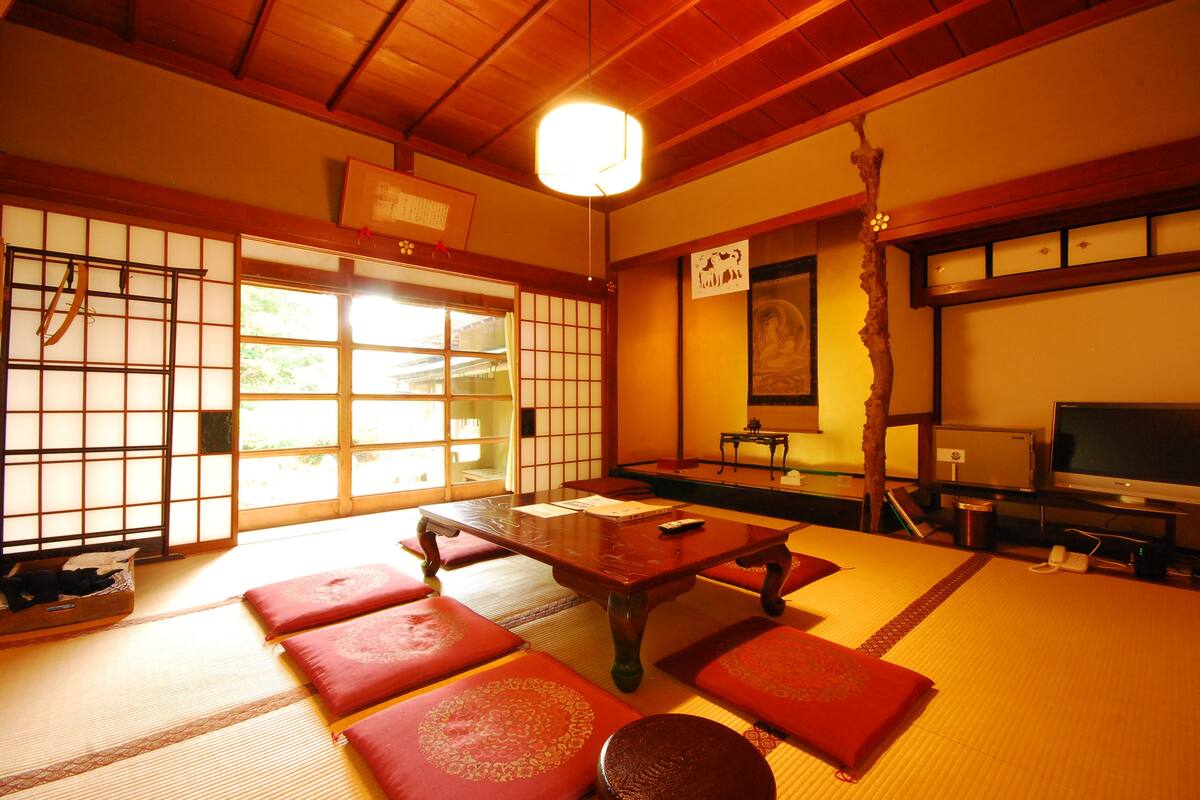 A traditional Japanese room with tatami flooring, a low wooden table, and red cushions.