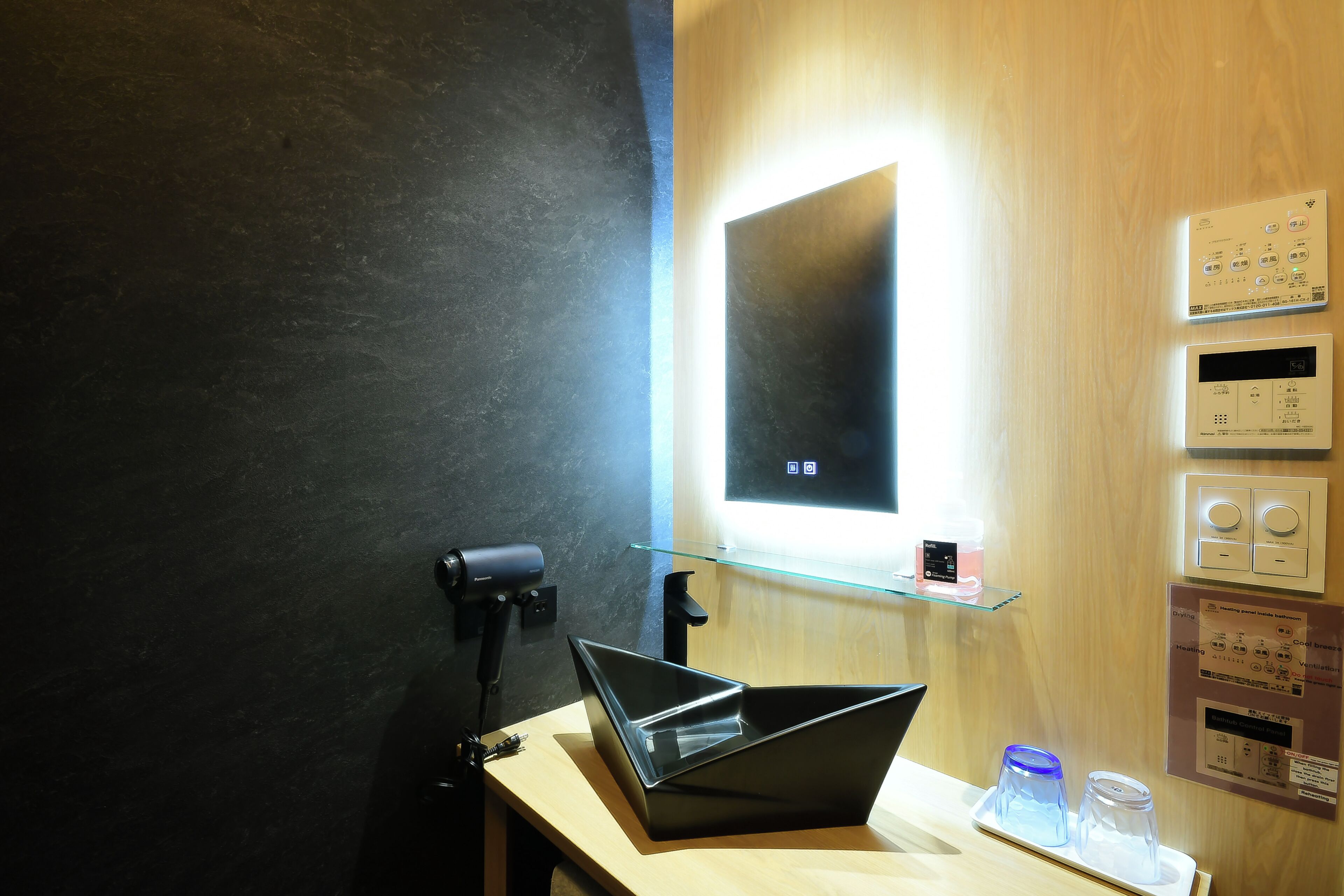 Un baño moderno con un lavamanos negro, un estante de vidrio y un espejo montado en la pared.