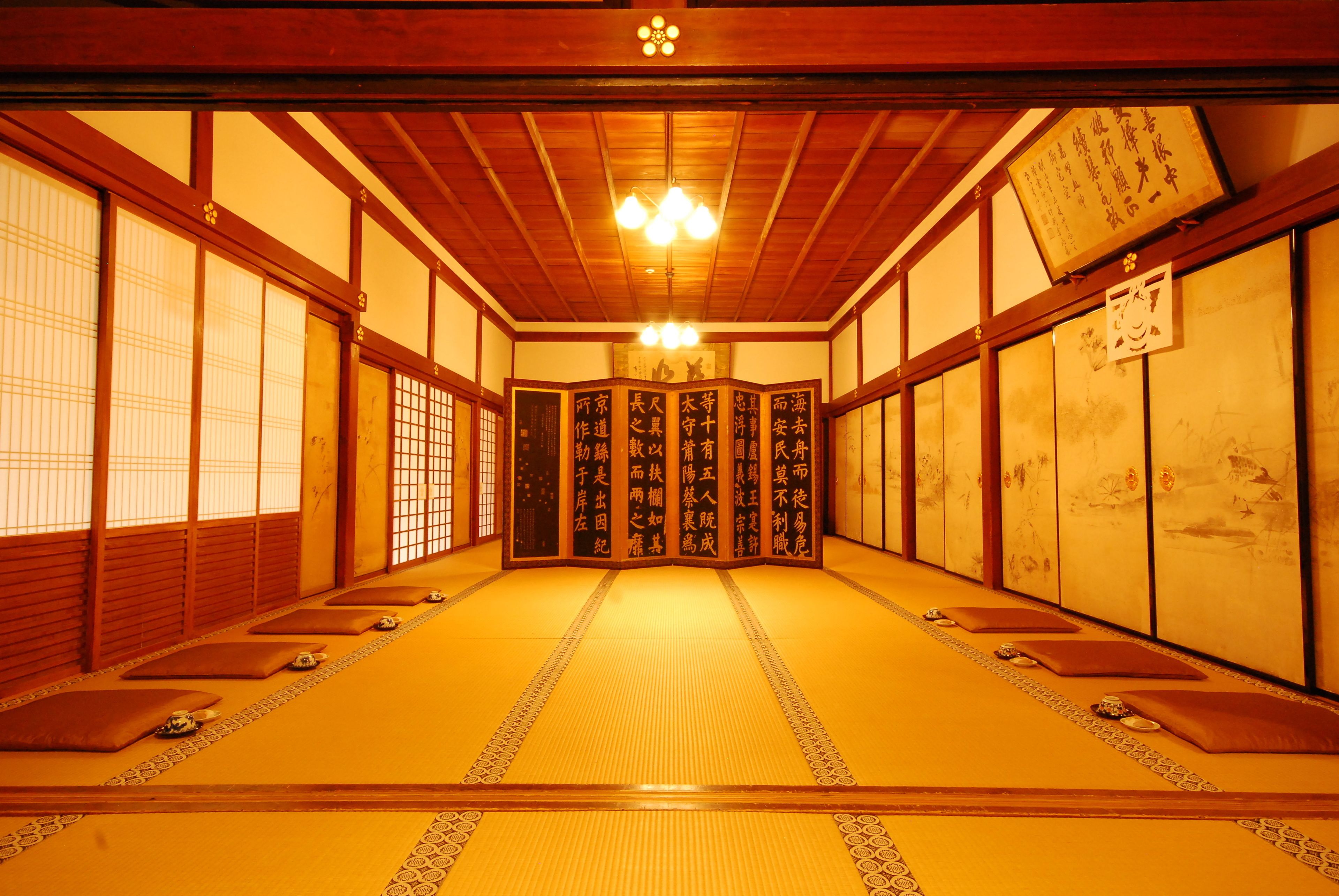 Ein traditioneller japanischer Raum mit Tatami-Boden, Schiebetüren und einer zentralen Säule mit Kalligraphie.