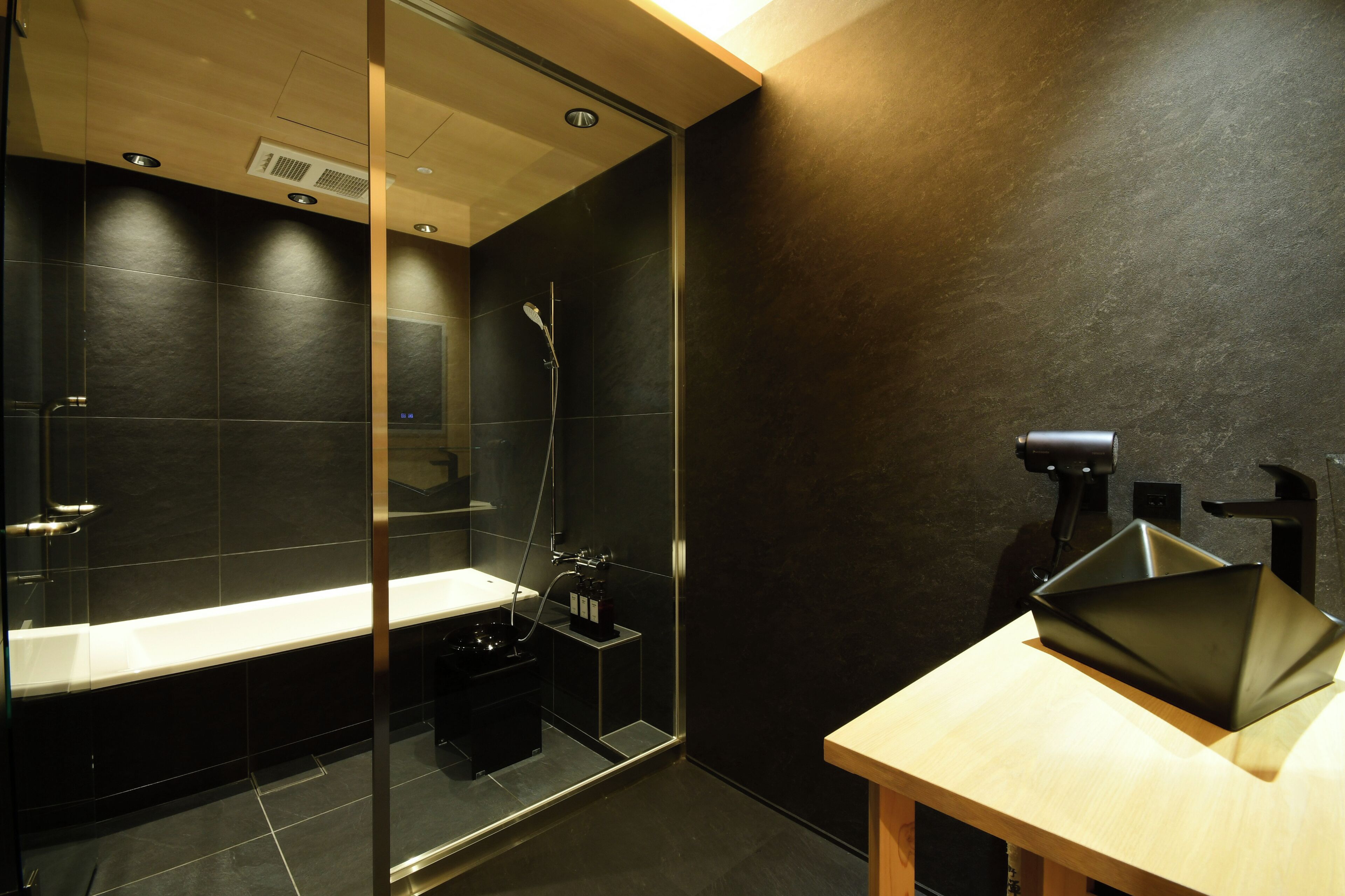 Un baño moderno con ducha de vidrio, tocador de madera y lavamanos negro.