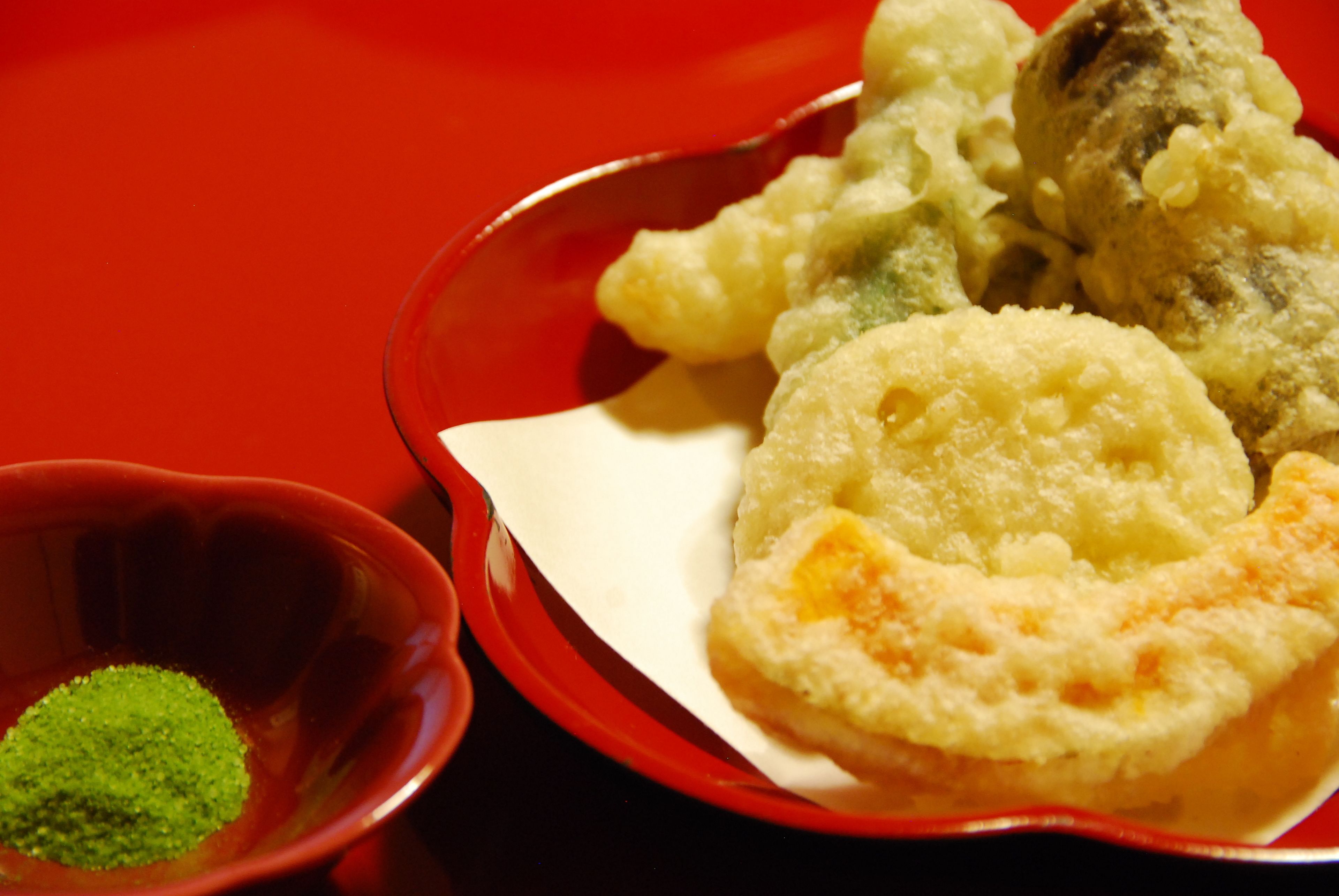 A red plate with various fried items and a small bowl of green powder.