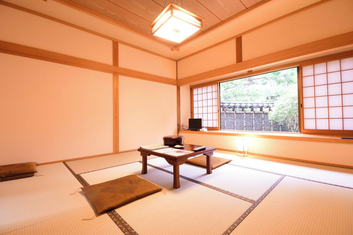 A traditional Japanese room with tatami flooring, a low wooden table, and a sliding door with a view of a garden.
