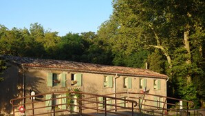 Um edifício rústico com telhado de cerâmica, venezianas verdes e um guarda-corpo metálico em frente.
