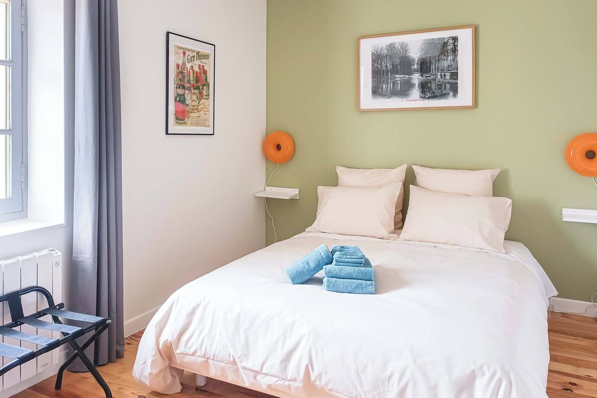 A bedroom with a bed, pillows, a chair, a radiator, and two wall-mounted lamps.
