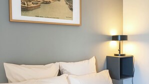 Cama bem arrumada com lençóis brancos, uma moldura com uma imagem de um canal e uma luminária moderna em uma mesinha de cabeceira.