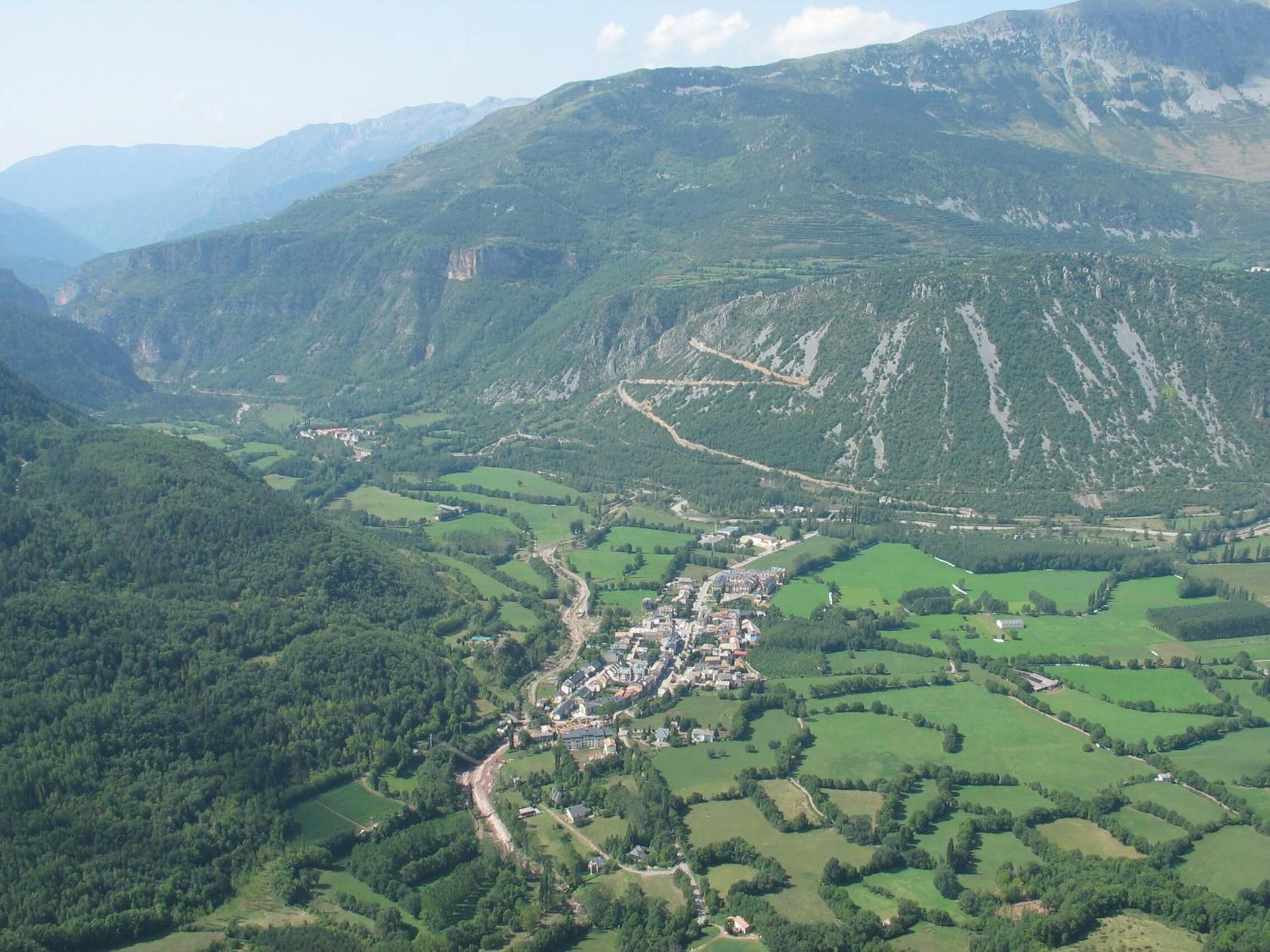 Un paysage montagneux avec une ville située dans une vallée, entourée de champs verdoyants et de zones boisées.