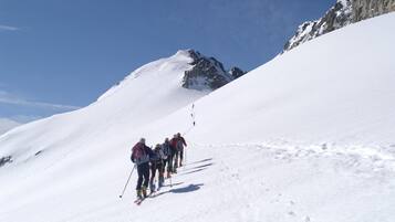 Un grupo de esquiadores asciende una ladera nevada con un pico montañoso rocoso al fondo.