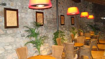 Un restaurante con mobiliario de mimbre, paredes de piedra y obras de arte enmarcadas.