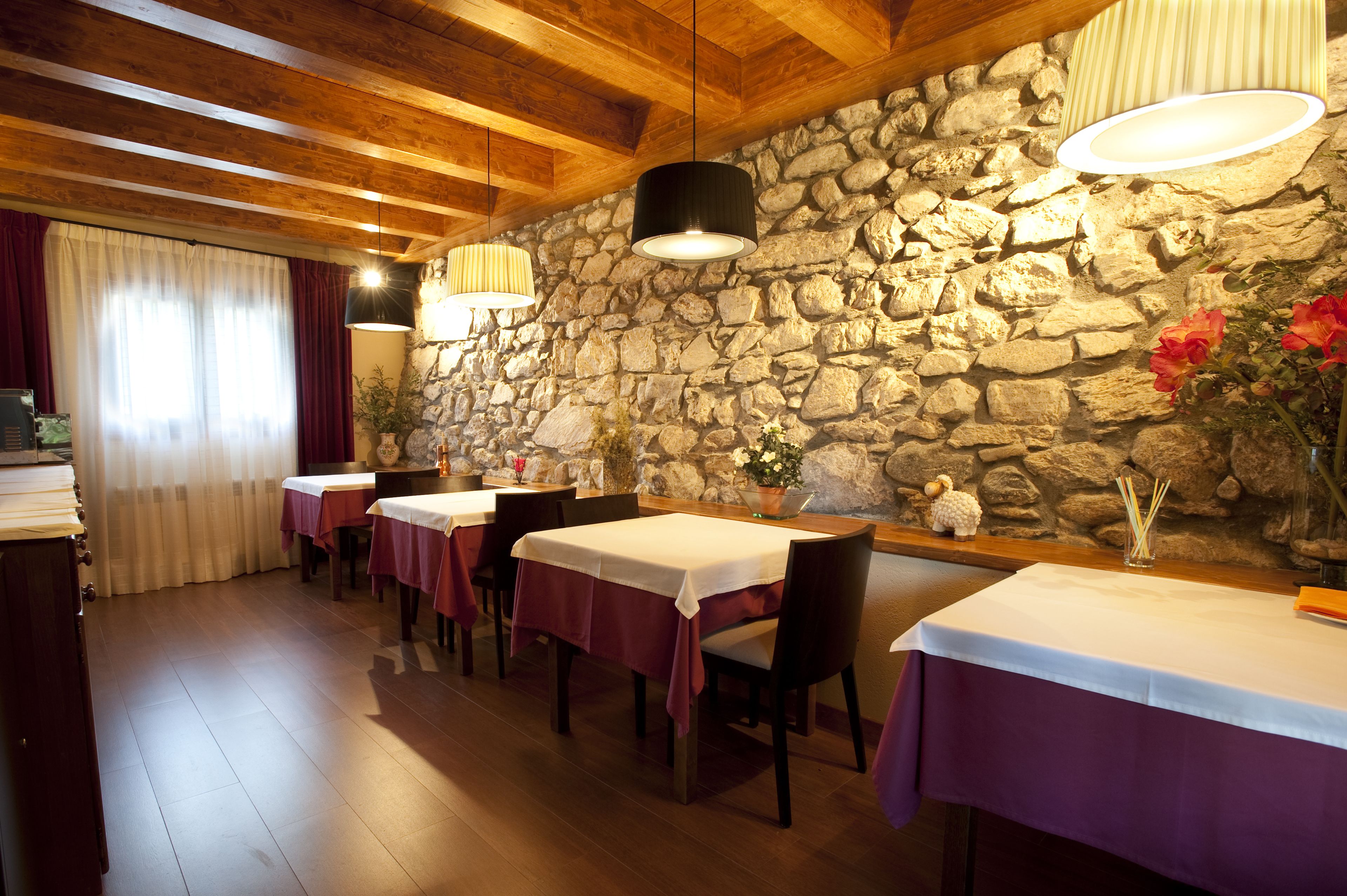 Un restaurante con paredes de piedra, vigas de madera en el techo y mesas dispuestas con manteles blancos y servilletas púrpuras.