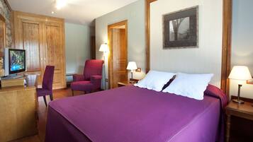 Quarto de hotel com uma cama grande, uma escrivaninha com televisão, uma poltrona vermelha e duas luminárias de cabeceira.