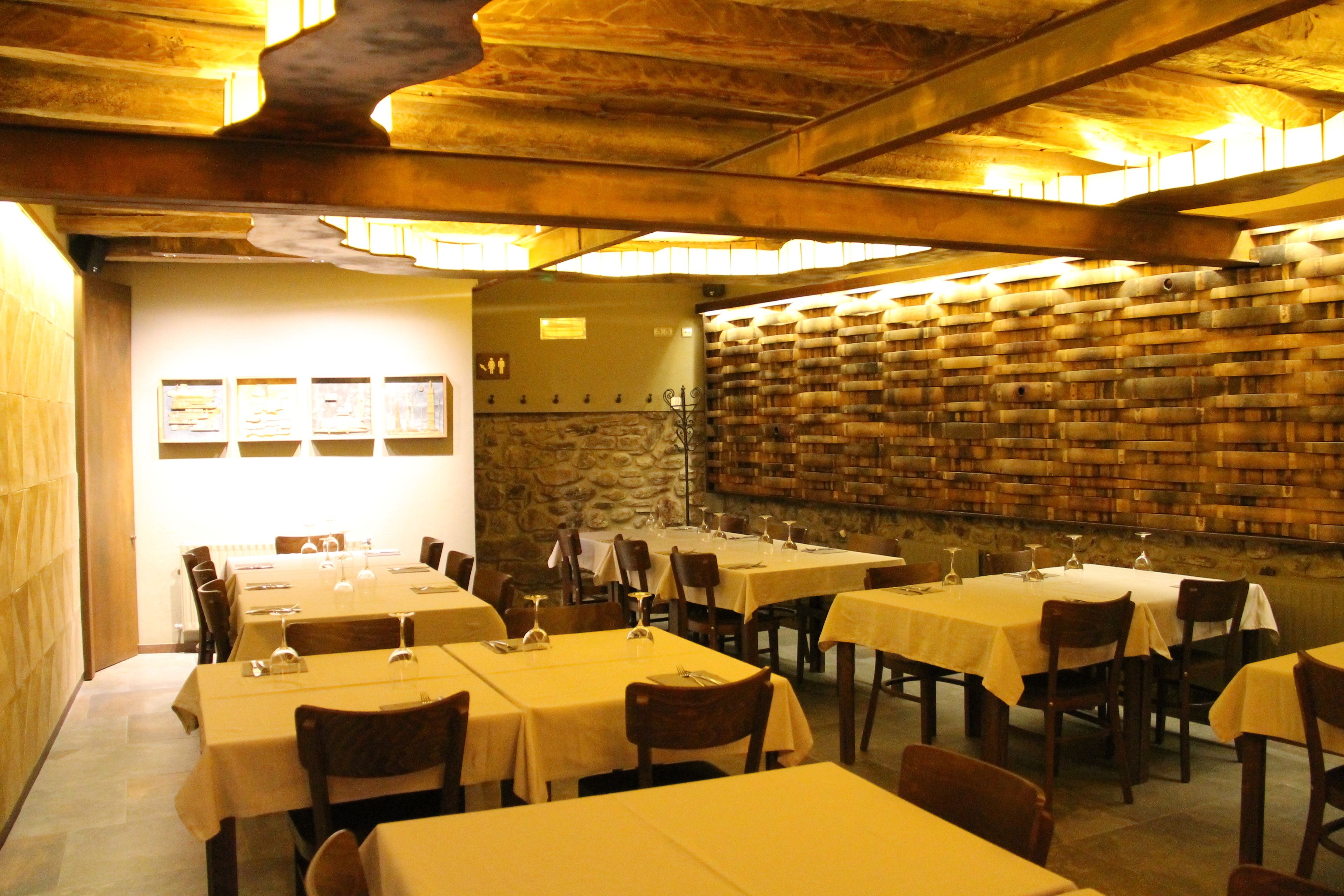 Un restaurant avec de nombreuses tables et chaises, un mur en pierre orné de barils et des tableaux encadrés.