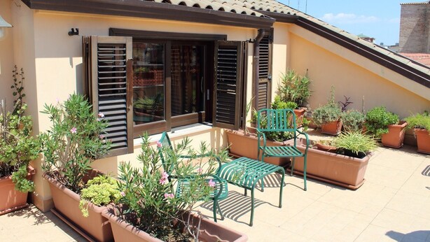 A building with a tiled roof, a balcony with green chairs and potted plants, and a window with shutters. - Centro Storico B&B (Foggia)