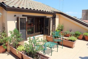 A building with a tiled roof, a balcony with green chairs and potted plants, and a window with shutters. - Centro Storico B&B (Foggia)
