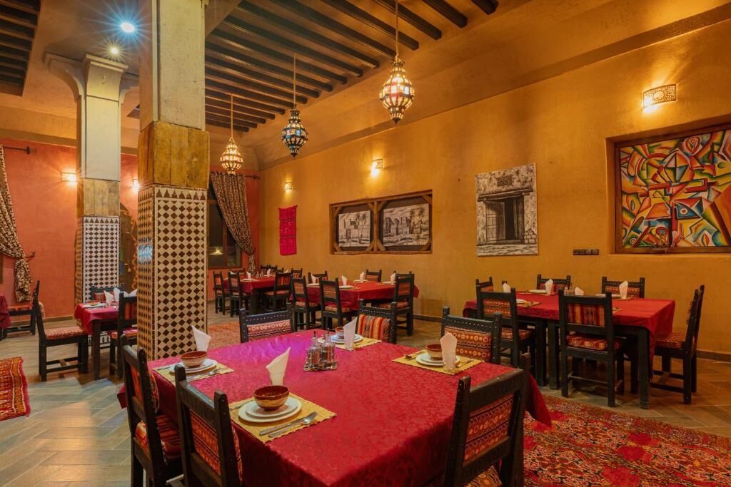 Un interior de restaurante con varias mesas, manteles rojos, decoración de pared estampada y lámparas colgantes.