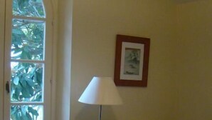 A room with a bed, a radiator, a lamp, a framed picture on the wall, and a window with greenery outside. - l'Oulibo (Villeneuve-les-Corbieres)