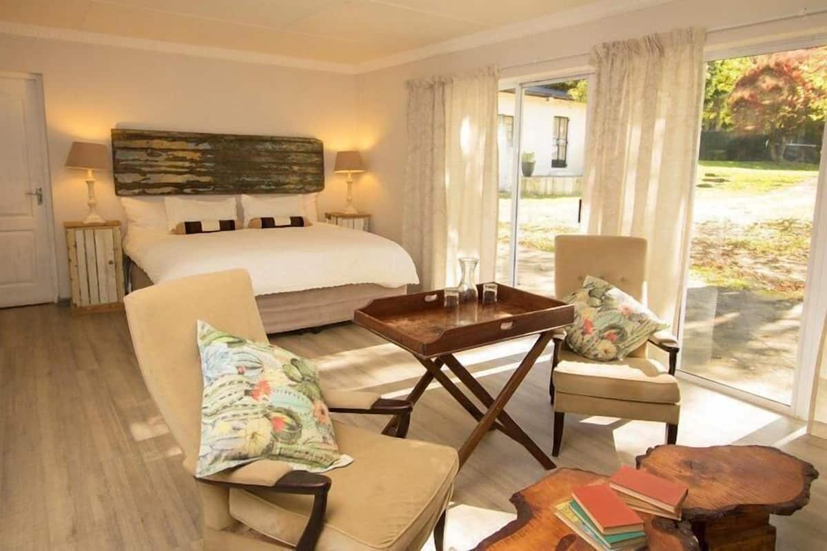 A bedroom with a bed, two chairs, a wooden table, and a view of the outdoors.