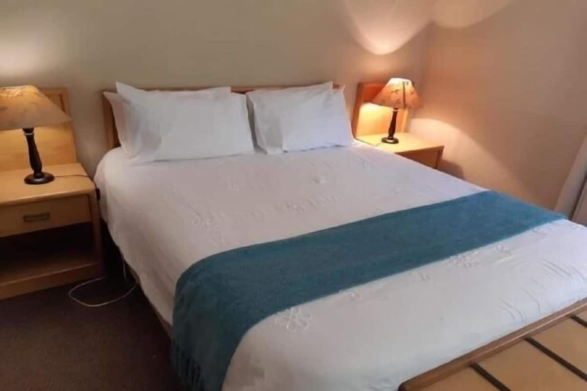 A neatly made bed with white linens and a blue accent, flanked by two bedside tables with lamps.