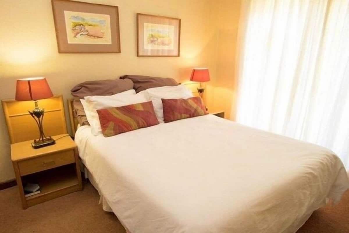 A hotel room with a bed, two bedside lamps, and two framed pictures on the wall.