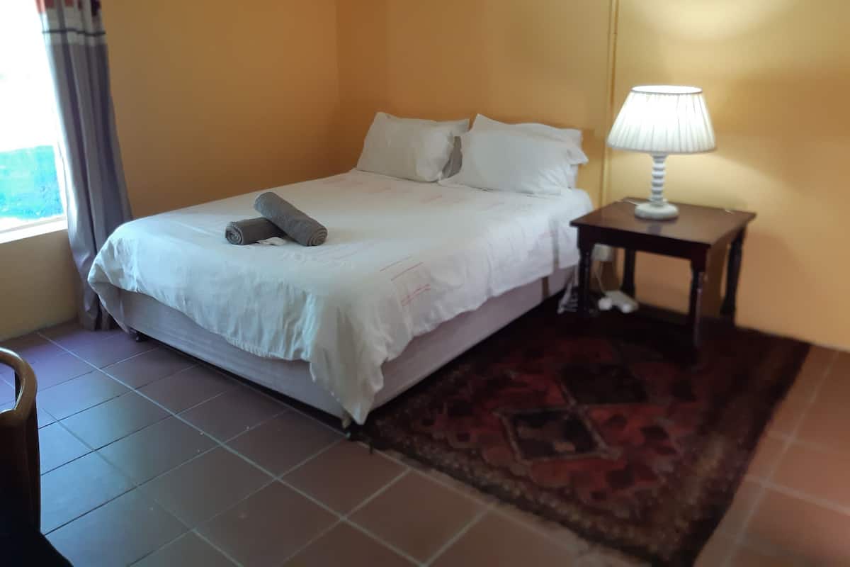A bed with white linens, a rolled towel, a bedside lamp, and a patterned rug.