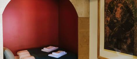 A small, cozy room with a single bed, a red wall, and a framed artwork on the wall.