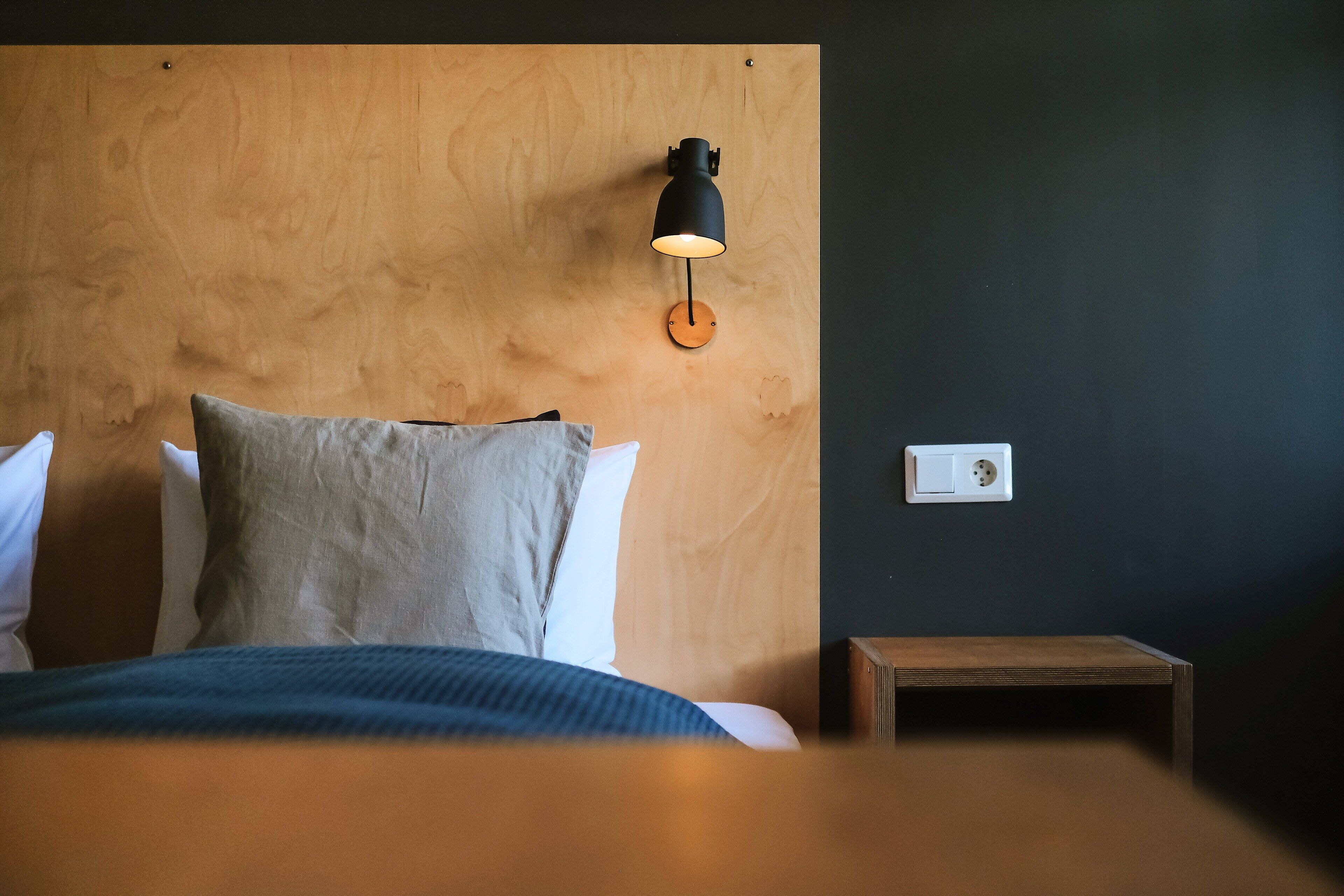 Un dormitorio con cabecera de madera, mesita de noche y lámpara de pared.