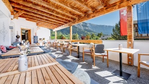 An outdoor seating area with wooden tables and chairs, overlooking a mountainous landscape. - Hapimag Resort Flims (Flims)