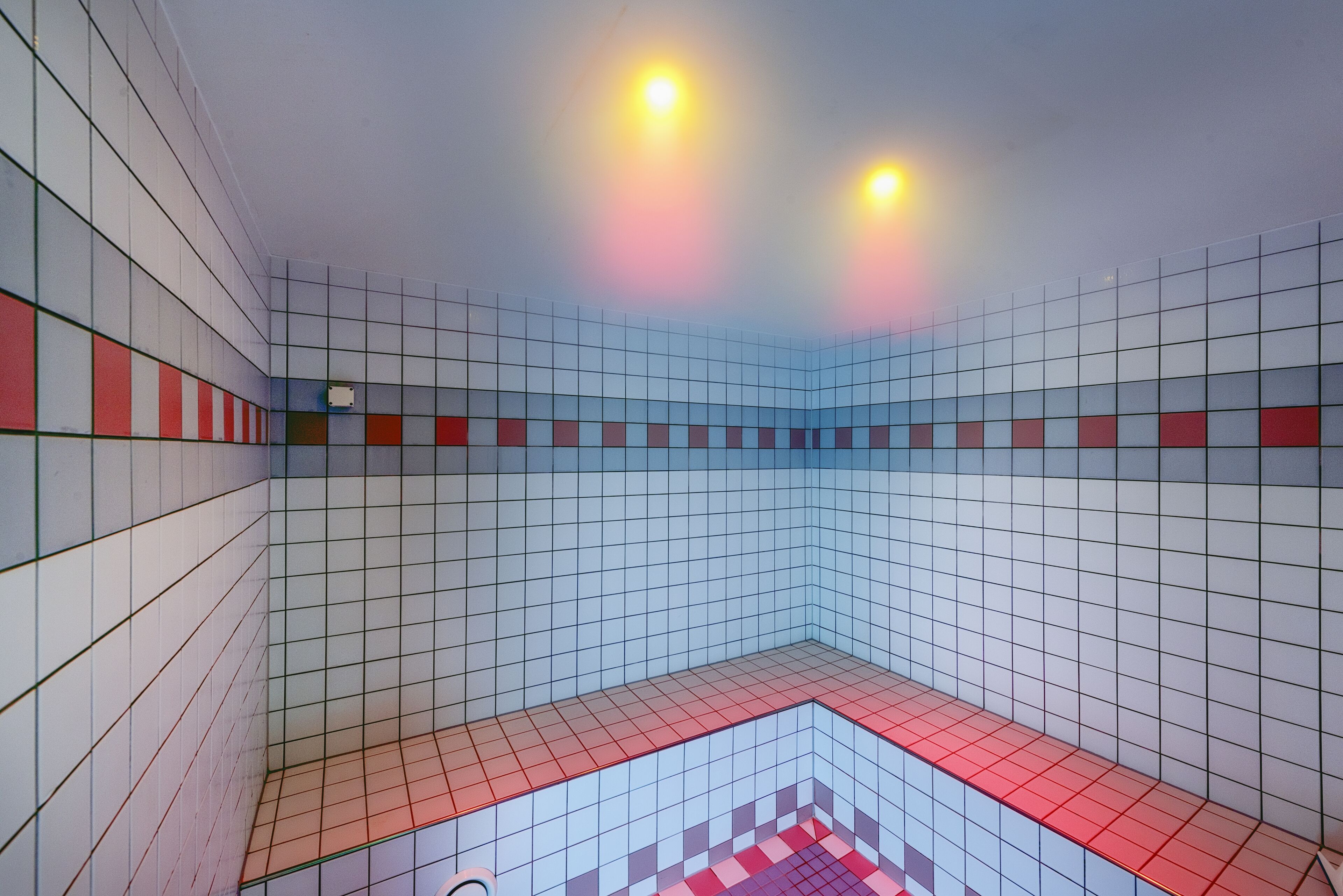 A tiled room with a red and white checkered floor pattern, a white ceiling, and two ceiling lights.