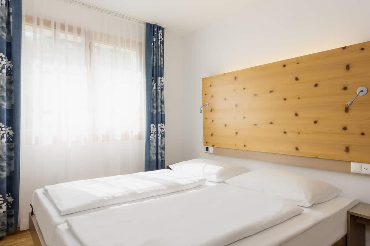 A double bed with white linens, a wooden headboard, and a nightstand with a lamp.
