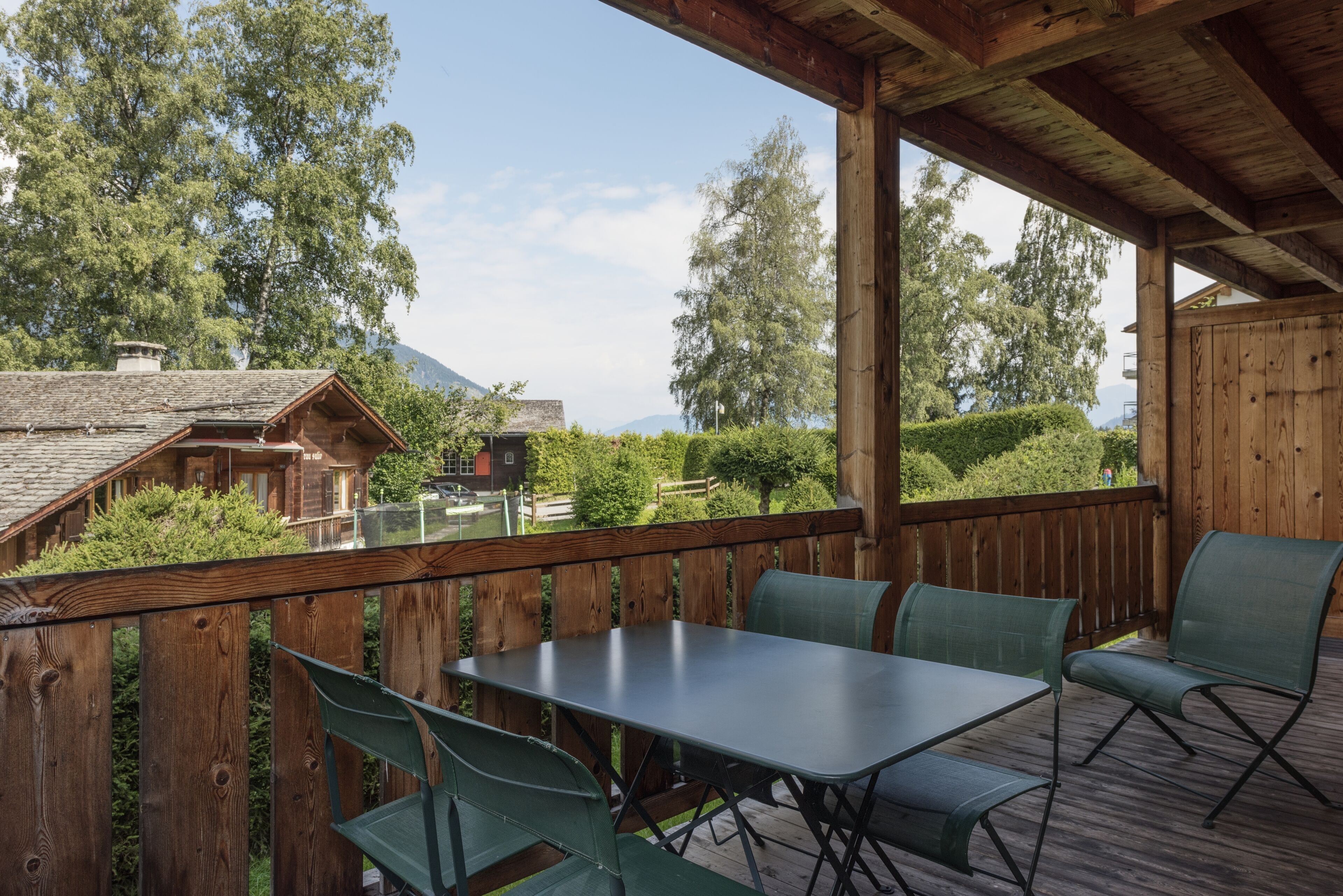 Un espace extérieur abrité, doté d’une table et de chaises, et entouré de rampes en bois et de verdure.