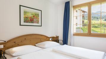 Ein Hotelzimmer mit einem Bett mit Holz-Kopfteil, einem gerahmten Landschaftsbild und einem Fenster mit Blick auf ein Gebäude und Grünflächen.