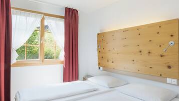 Un dormitorio con dos camas individuales, cabecero de madera, ventana con cortinas rojas y vista a la vegetación.