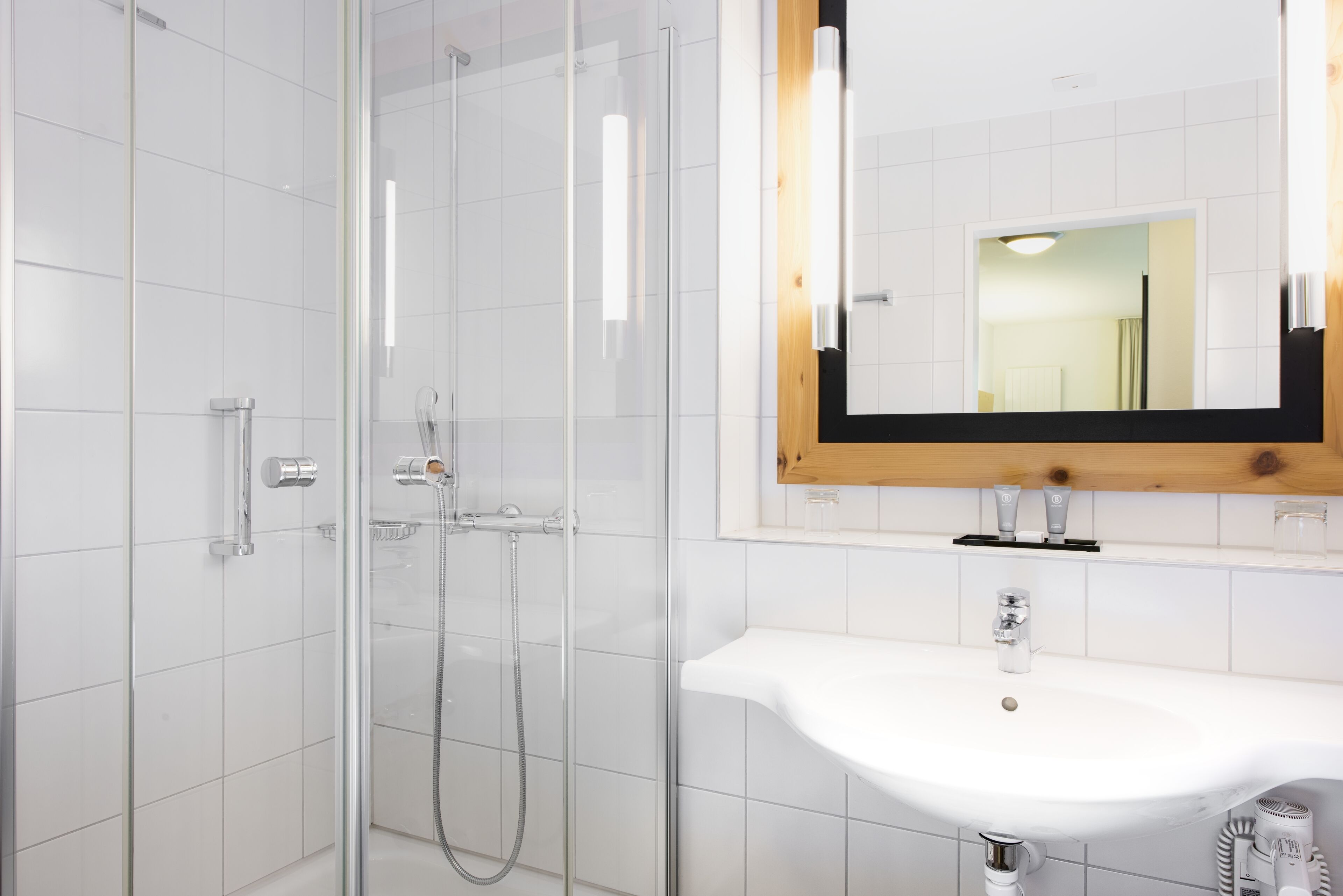 A modern bathroom with a glass-enclosed shower, a white sink, and a mirror with a wooden frame.