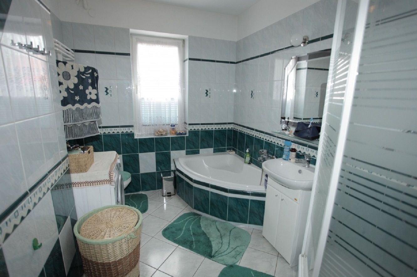 Une salle de bain avec une baignoire, un lavabo et un miroir. Il y a une fenêtre avec un rideau, et les murs sont recouverts de carreaux.